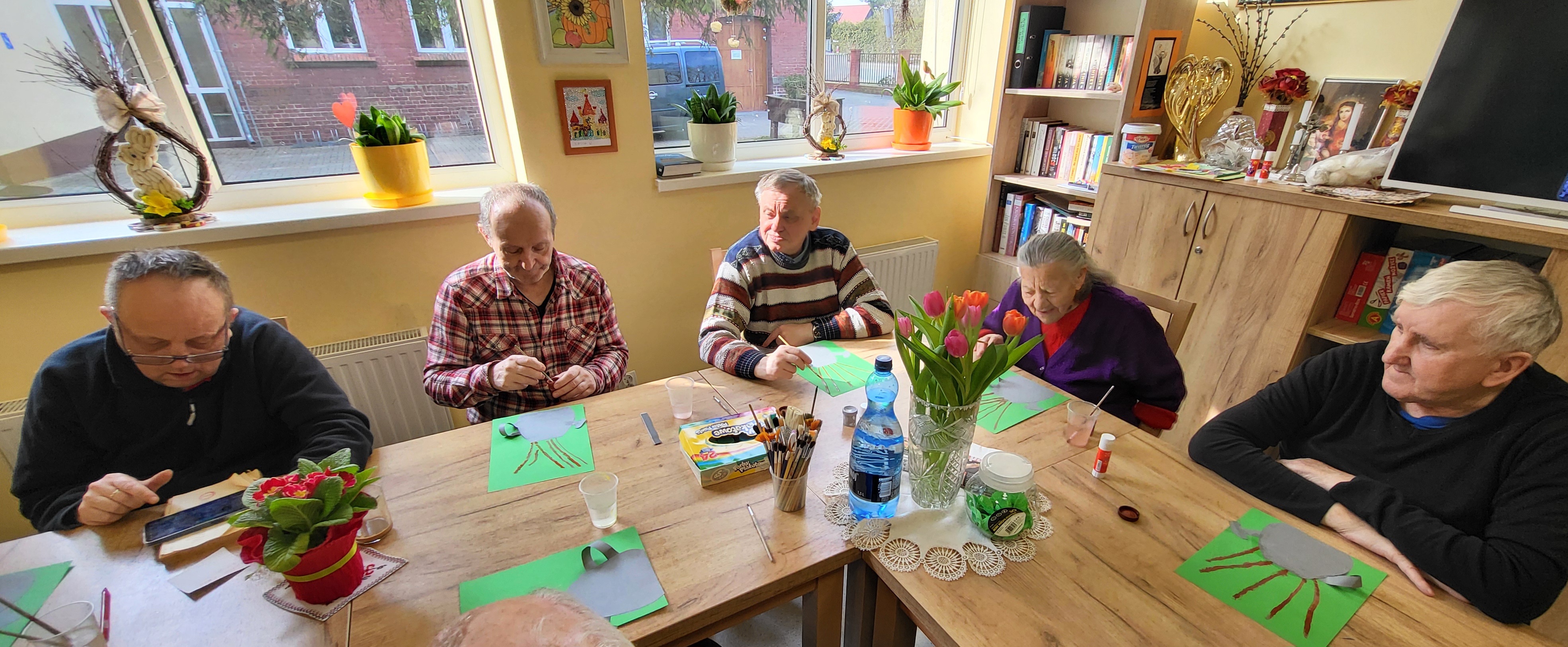 Mieszkańcy DPSu siedzą przy stole i tworzą wiosenne prace plastyczne